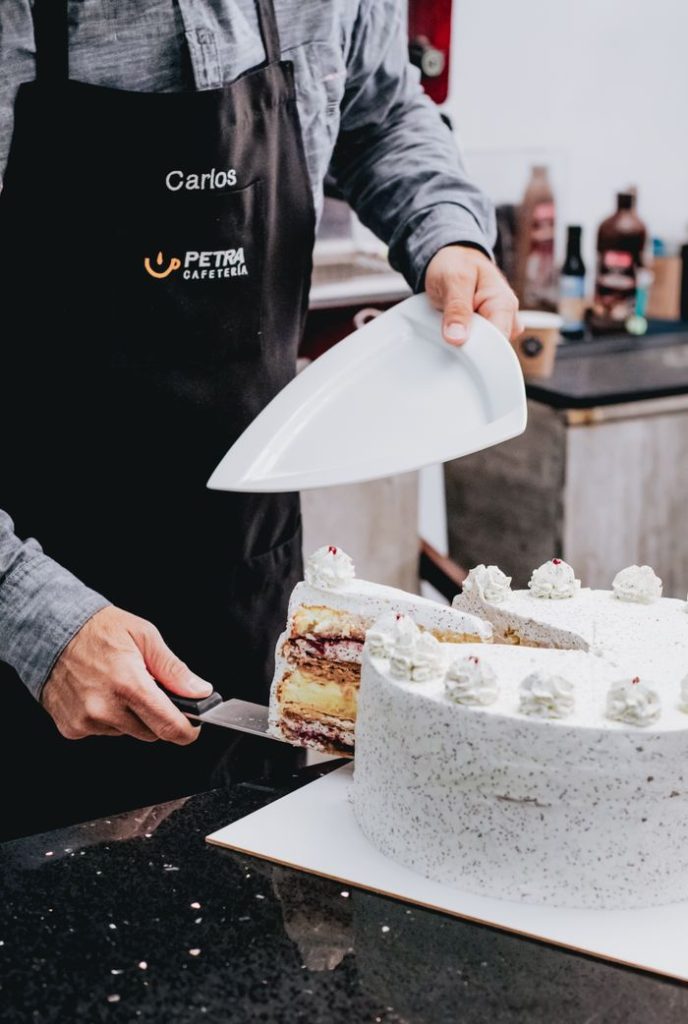 Barista slicing a white cream cake in a cozy café, showcasing a warm coffee shop atmosphere.