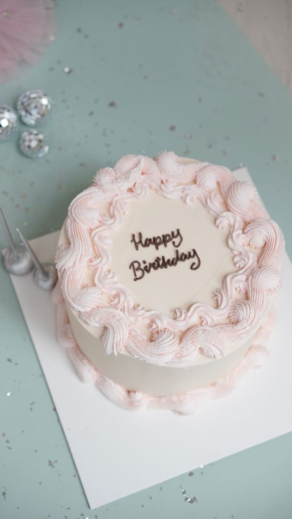 A beautifully decorated pink and white birthday cake with elegant piping detail.